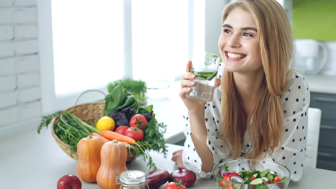 Woman on a diet. Young and happy woman eating healthy salad sitting on the table with green fresh ingredients indoors. High quality photo